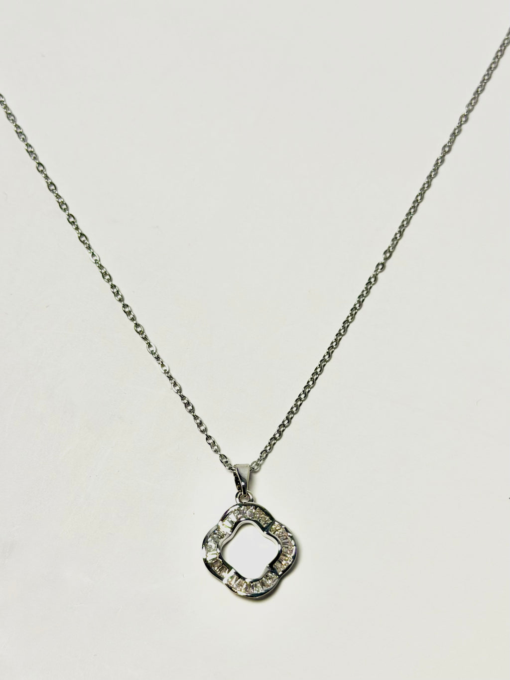 A silver-tone necklace with a delicate chain and a geometric, open quatrefoil pendant embellished with small clear stones, shown against a plain light background.