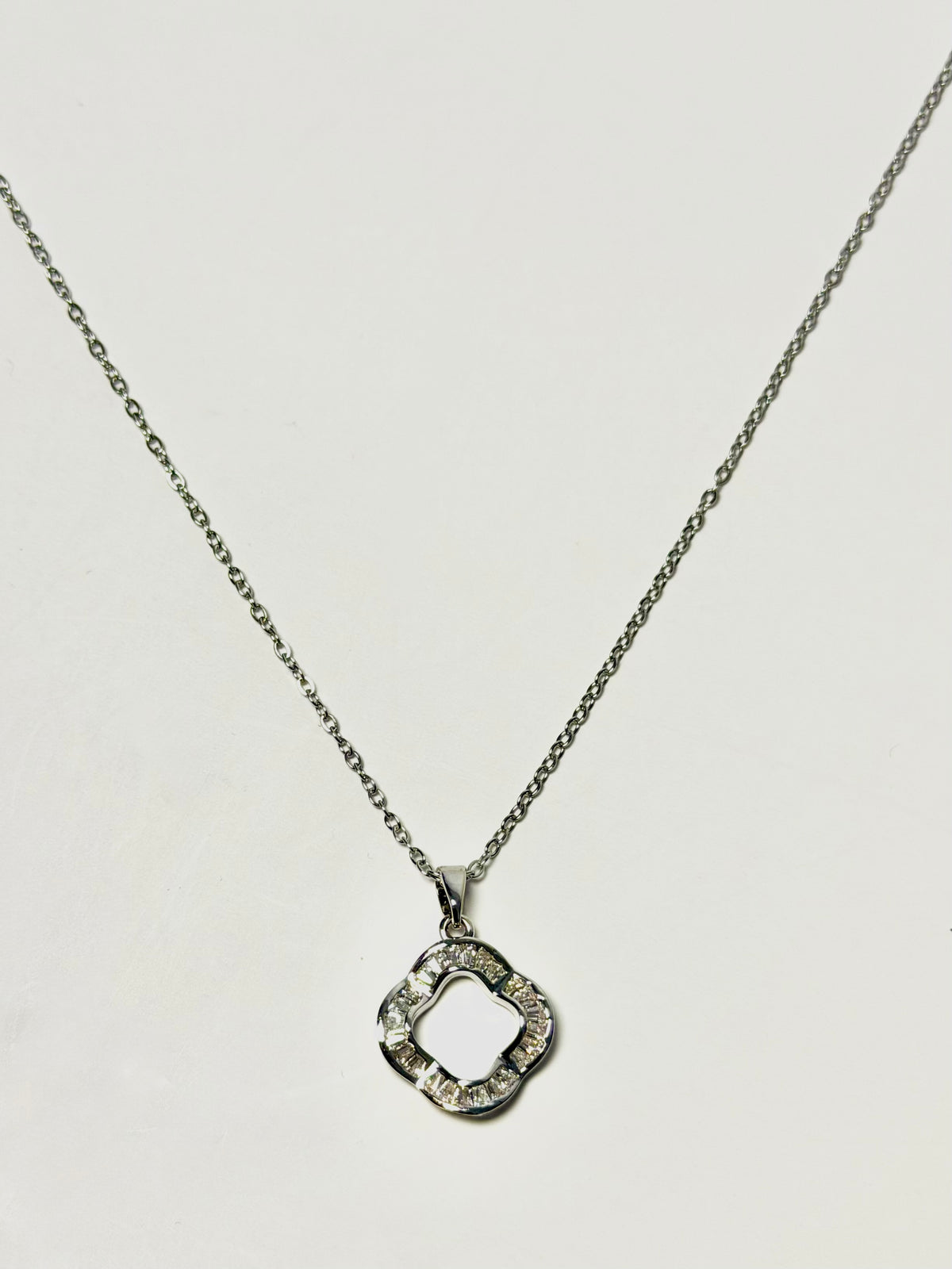 A silver-tone necklace with a delicate chain and a geometric, open quatrefoil pendant embellished with small clear stones, shown against a plain light background.